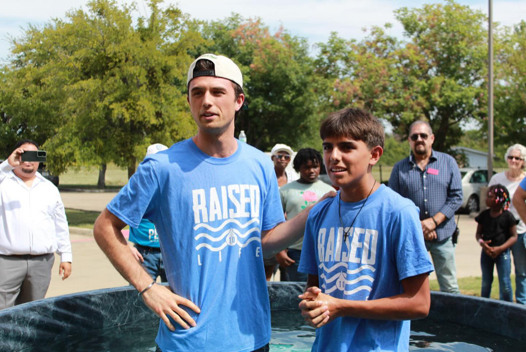 Two people standing in a pool of water wearing blue shirts that say raised to life.